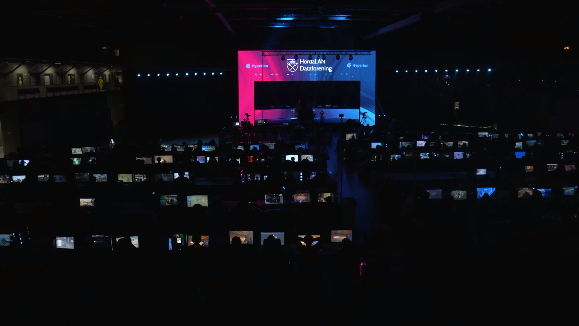 Dataskjermer og en skjerm som lyser opp et stort mørkt rom.